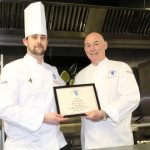 Entier’s Executive Chef Inducted into the Master Chefs’ Hall of Fame George McIvor, National Chairman of Master Chefs of Great Britain (right) in Entier’s Training Academy kitchen presenting much sought after Master Chef’s white jacket and member certificate to Alisdair Macsween, Entier Executive Chef (left).